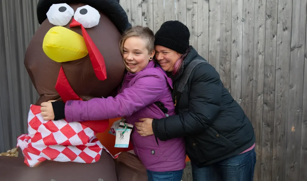 Feeding Champlain Valley Holidays without Hunger photograph of a mother and daughter hugging a Thanksgiving Turkey decoration outside the Burlington Food Shelf.