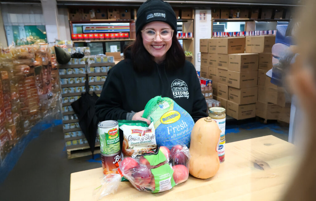 Photograph of woman in a black Feeding Champlain Valley sweatshirt with donated turkeys and other food.